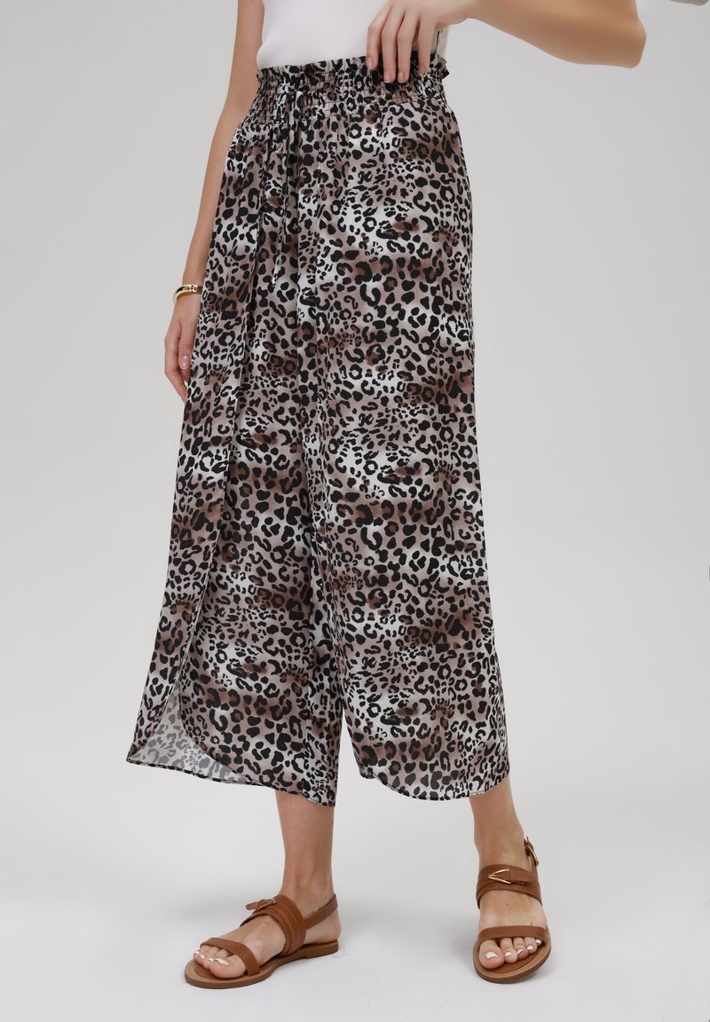 Pantalons larges à imprimé léopard en tissu léger avec une taille élastique. Palette de couleurs brun, noir et crème. Sandales plates portées.