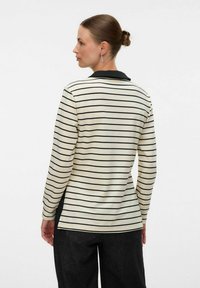 Camicia a maniche lunghe a righe in crema e nero, con colletto nero e spacchi laterali, realizzata in un tessuto morbido con vestibilità comoda.
