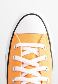 Oranžové plátěné tenisky s bílou gumovou špičkou, černým lemem a bílými tkaničkami protaženými stříbrnými očky. Texturovaná látka a klasický design.