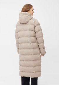 Beige lang pufferjakke med hætte, prydet med et quiltet design, blød tekstur og trykknaplukninger. Ideel til koldt vejr.