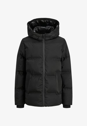 Must kapuutsiga ja eesluku pandlaga puffer jope, kombineeritud heleda särgi ja laia pruuni korduroopükstega. Paistavad valged tossud.