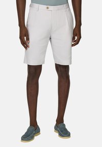 Shorts en coton blancs avec une taille plate, deux poches latérales et un unique bouton à l'avant. Portés avec des chaussures en daim bleu à enfiler.