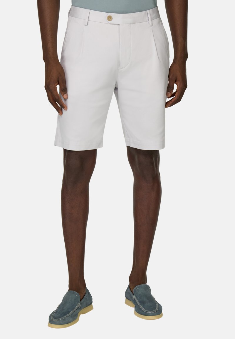 Shorts en coton blancs avec une taille plate, deux poches latérales et un unique bouton à l'avant. Portés avec des chaussures en daim bleu à enfiler.