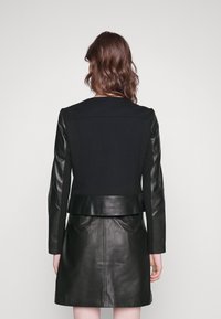 Giubbotto nero con maniche in pelle e taglio slim, caratterizzato da una texture liscia e un design sartoriale, che termina sopra la vita.