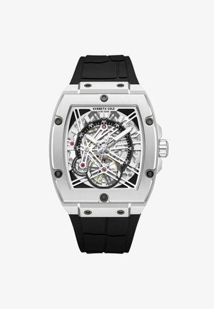 Skeleton automatic watch with a silver stainless steel case, black rubber strap, and intricate white and yellow detailing on the face.