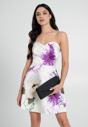 Schulterfreies Blumenkleid aus weißem Stoff mit lila und grünen Akzenten. Begleitet von einer schwarzen Clutch mit strukturiertem Oberflächen.