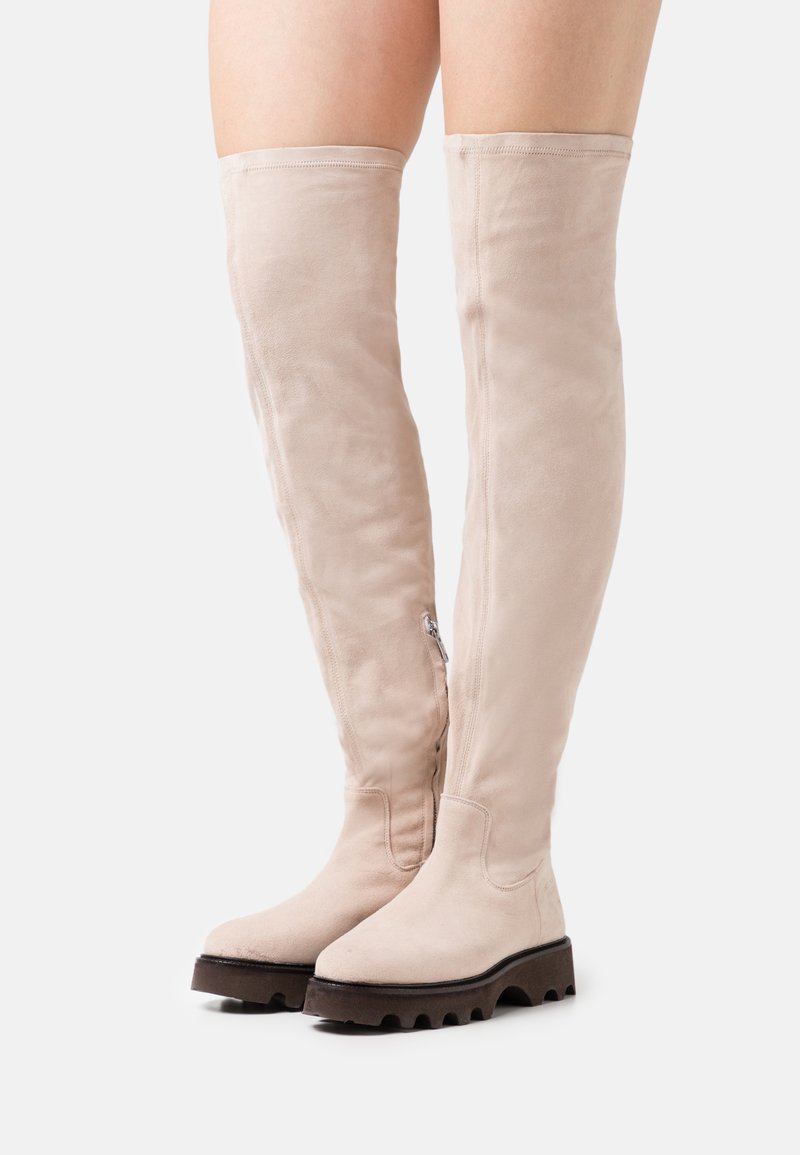 Beige Wildleder-Stiefel über das Knie mit runder Zehenform und grober schwarzer Gummisohle. Sie verfügen über einen seitlichen Reißverschluss und eine glatte Textur.