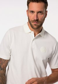 Polo bianca realizzata in tessuto testurizzato, con un logo ricamato discreto sul petto e un design del colletto classico.