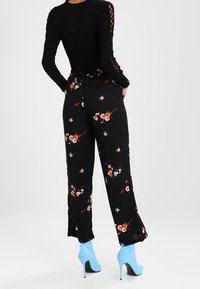 Pantalons floraux noirs à coupe ample, avec un motif floral multicolore. Associés à des talons hauts bleu ciel et un top noir ajusté avec découpes.