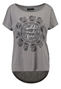 Camiseta gris de manga corta, con cuello redondo y un respaldo más largo. Presenta un patrón floral negro con el texto "salvaje y libre" en blanco.