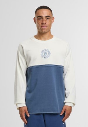 Felpa leggera color crema e blu marina con colletto a girocollo, caratterizzata da un logo circolare sul petto e cuciture a contrasto lungo l'orlo.