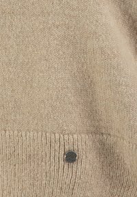 Maglione beige in maglia con orlo a coste e un piccolo tag metallico con un design a forma di cuore cucito sul lato anteriore.