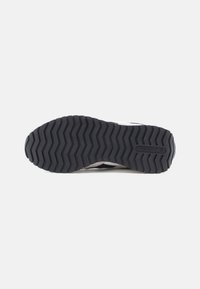Crna gumena potplat s dubokim cik-cak uzorkom i Reebok logom na peti, prikazana s donje strane na bijeloj pozadini.