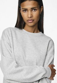 Sudadera gris con cuello redondo, mangas largas y una textura suave. La tela parece ligeramente jaspeada con detalles de costura visibles.