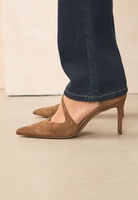 Rudos zomšos aukštakulniai bateliai su smailia nosimi ir atvira kirpimo detale, derinami su tamsios spalvos džinsais tiesios kojos siluetu.