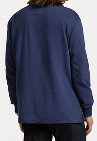 Merivoimien pitkähiha shirtti pehmeästä kankaasta. Ominaisuuksiin kuuluu pyöreä pääntie, sivuaukot ja rento istuvuus. Sujuva pinta yksinkertaisella muotoilulla.