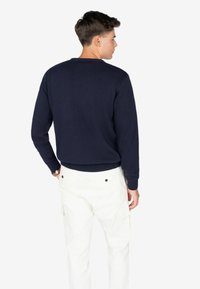 Suéter de punto azul marino con cuello redondo, puños acanalados y dobladillo. Combinado con pantalones cargo blancos con bolsillos laterales y detalle de botón en la parte trasera.
