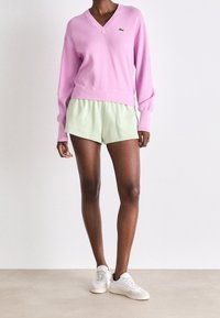 Jersey de pico rosa con mangas largas, combinado con unos pantalones cortos verde claro. Zapatillas blancas completan el look. Diseño simple y casual.