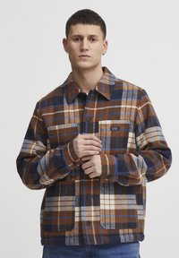 Brown and navy plaid shirt jacket, featuring a button-up front, collar, chest pocket, and a soft, textured fabric with contrasting colors.