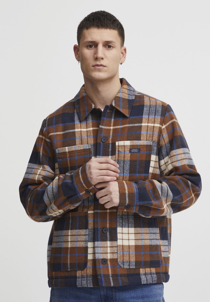 Brown and navy plaid shirt jacket, featuring a button-up front, collar, chest pocket, and a soft, textured fabric with contrasting colors.
