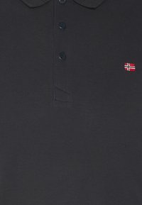 Polo-shirt marine avec col, comportant trois boutons et un petit emblème en rouge et blanc du drapeau norvégien sur la poitrine à gauche.