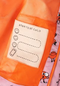 Tissu en maille orange avec une étiquette cousue présentant trois visages souriants et une icône de téléphone. L'étiquette indique "NÉ POUR ÊTRE ENFANT."