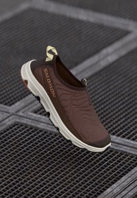 Hnědé nazouvací boty s texturovaným svrškem, vybavené světlou podešví a výrazným logem na boku. Robustní design pro venkovní použití.