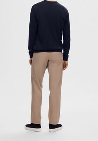 Tmavě modrý svetr s kulatým výstřihem, béžové kalhoty a černé slip-on tenisky. Outfity jsou neformální s volným střihem a hladkými texturami.