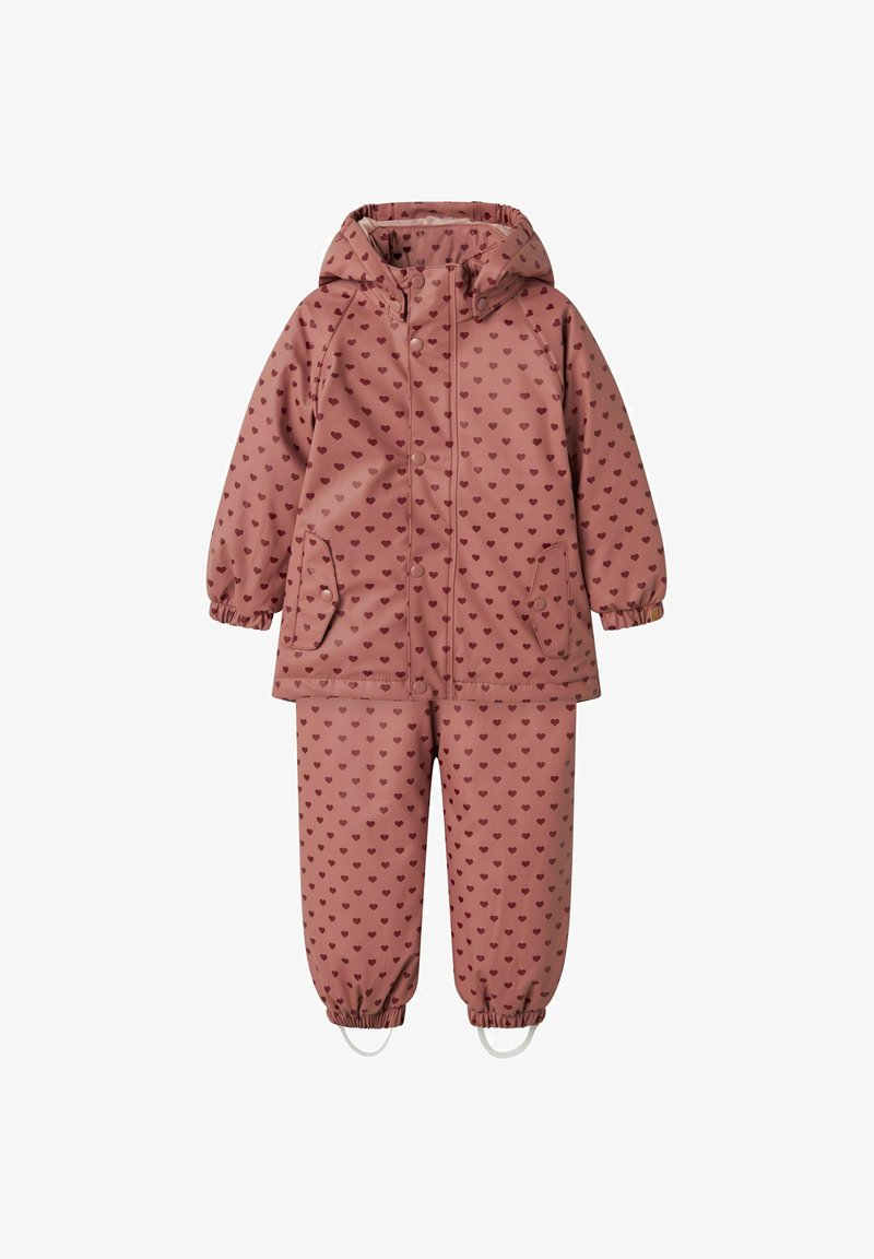 Ensemble de veste et pantalon imperméable rose pour enfant avec des motifs de cœurs bordeaux, des poignets élastiques, une capuche et des étriers sur le pantalon.