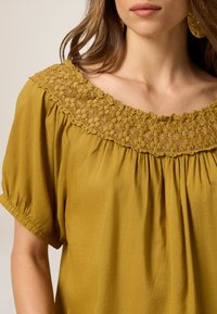 Mosterdgele blouse met een gestructureerde, geborduurde bloemenhalslijn en korte, verzamelde mouwen. Zachte stof met eenRelaxte pasvorm.
