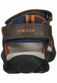 Sandalia azul y naranja con una correa de cuero marrón, suela de goma texturizada, cierre de velcro y tejido perforado para transpirabilidad.