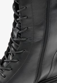 Stivale in pelle nera con lacci, dotato di una zip laterale, dalla consistenza morbida, con cuciture sottili e punta tonda, completo di una suola in gomma flessibile.