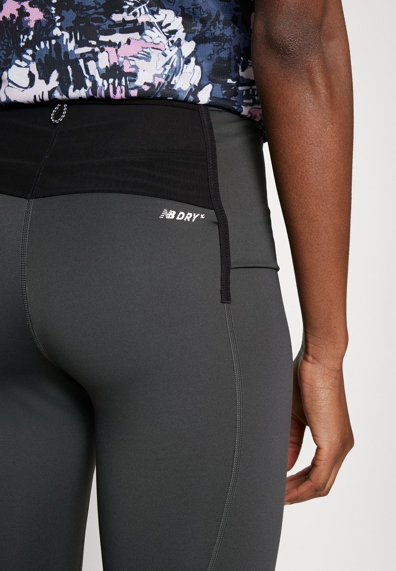 Leggings de sport noirs avec une texture lisse, présentant une taille haute et un logo "NB DRY" en blanc. Le gros plan montre une partie d'un haut à motifs.