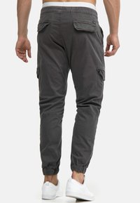 Graue Cargo-Hosen mit einem elastischen Bund und zwei Seitentaschen. Schmal zulaufendes Bein, das in Bündchen endet. Kombiniert mit weißen Sneakers.