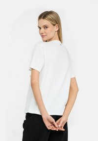 T-shirt bianco a maniche corte con scollo rotondo, caratterizzato da un sottile dettaglio sul retro e una vestibilità comoda. Il tessuto appare liscio e leggero.