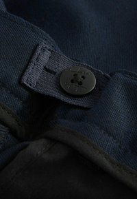 Navyblauw stof close-up met een zwarte knop met reliëflogo. De textuur lijkt glad te zijn met zichtbare stiksels rond de randen.