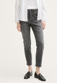 Jeans de denim gris con un ajuste slim y longitud hasta el tobillo, que presentan un diseño clásico de cinco bolsillos y una sutil textura desgastada. Combinados con mocasines negros.