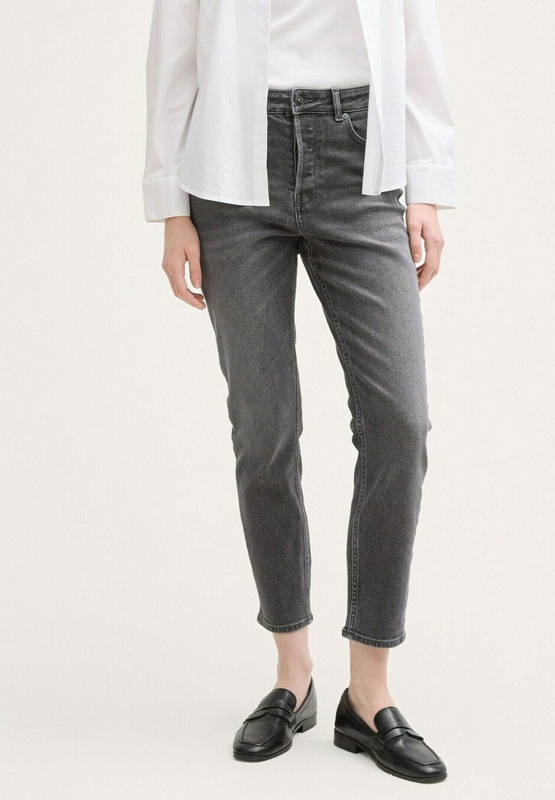 Jeans de denim gris con un ajuste slim y longitud hasta el tobillo, que presentan un diseño clásico de cinco bolsillos y una sutil textura desgastada. Combinados con mocasines negros.