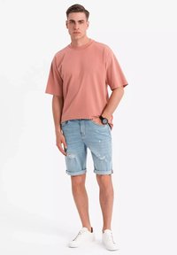 Ljusrosa t-shirt med kort ärm, ljusblå slitna denimshorts med uppkavlade ärmslut och vita sneakers. Enkel design och avslappnad passform.