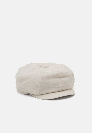 Casquette en lin beige clair avec un dessus rond et un bord légèrement allongé. Présente un bouton central et des détails cousus pour une texture supplémentaire.