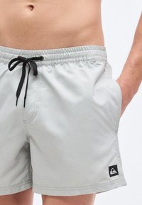 Ανοιχτό γκρι μαγιό σορτς από λείο ύφασμα με ελαστική μέση και μαύρο κορδόνι. Διαθέτει πλαϊνές τσέπες και λογότυπο.