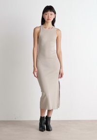 Rochie midi bej fără mâneci, cu fante laterale, textură netedă, siluetă ajustată, asortată cu botine negre, pe un fundal neutru.