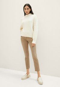 Pull à côtes crème avec col montant, associé à un pantalon beige ajusté et des mocassins crème. Design simple avec un tissu texturé.