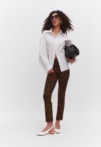Valkoinen napillinen paitapusero puffi-hihalla, ruskeat tiikerikuosiset leggingsit ja valkoiset avokkaat, joissa on vaalea korostus; pitämällä mustaa clutch-laukkua.