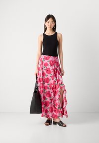 Débardeur noir avec une jupe maxi à fleurs roses, ornée de volants et d'une fente sur le côté. Les accessoires comprennent un sac fourre-tout noir et des sandales à talons blocs.