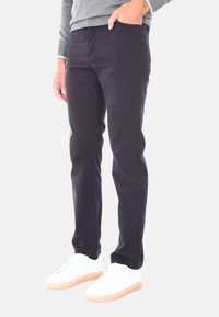 Pantaloni di cotone blu scuro con una vestibilità slim, dotati di tasche laterali, dettagli di cucitura discreti e indossati con sneakers bianche.