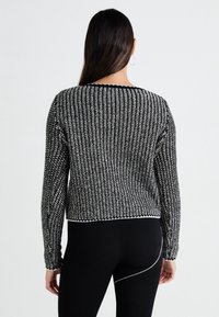Pull tricoté en noir et blanc avec un motif texturé, col rond et manches longues, avec un ourlet et des poignets côtelés.