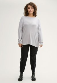 Lichtgrijs langemouwen top met een relaxte pasvorm en een ronde halslijn, gecombineerd met zwarte tapered broek en enkellaarsjes met een stevige zool.