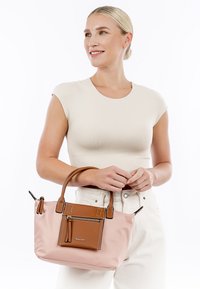 Hellrosa Tragetasche mit einer braunen strukturierten Fronttasche, doppelten Griffen, Reißverschlussdetails und kontrastrierenden Nähten. Glatte Materialoberfläche.