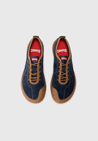 Navy suede shoes with brown laces and rubber soles. Red interior featuring 'CAMPER' branding. Rounded toe and textured surface.
